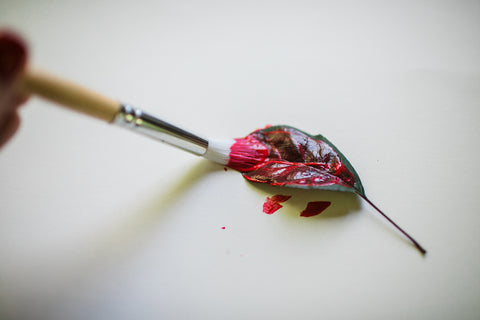 Paintbrush painting red paint on a leaf