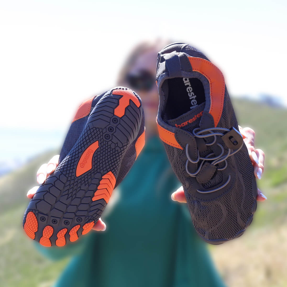A woman raising and holding a pair of Barestep Active 2.0 barefoot shoes.