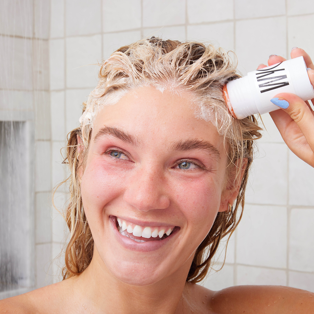 Young woman smiling while shampooing her hair in the shower.