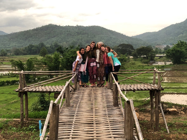Girls smiling and hugging on a wooden bridge in the Thai jungle after meeting on a small group trip.