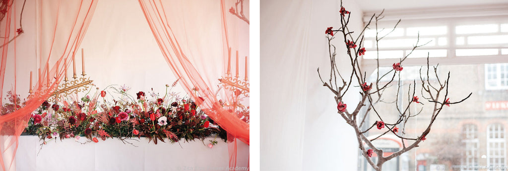 red and burgundy flower arrangement on a white table with candelabra and red curtains