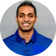 A person smiling in a blue collared shirt against a neutral background.