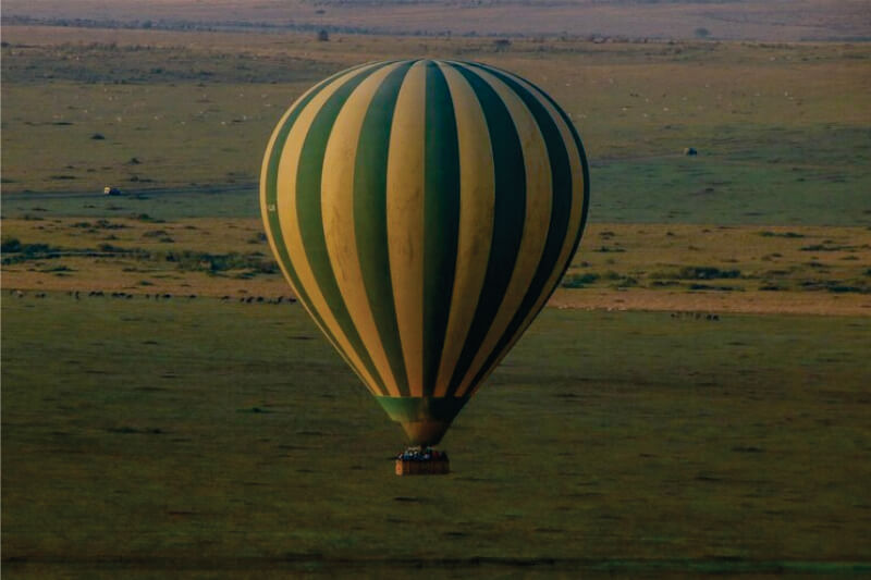 Gruppe von Menschen, die in einem grün-gelben Heißluftballon über die Masai Mara-Ebenen auf einer Masai Mara-Ballonsafari für kleine Gruppen fliegen