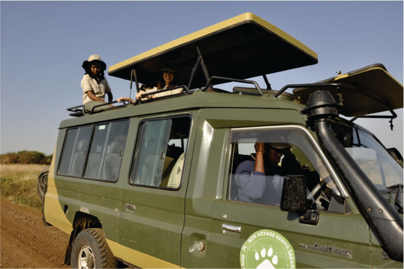 Deux guides de voyage du voyagiste Bon Voyage Budget Safari au Kenya profitant de safaris dans une jeep 4x4 verte avec toit ouvrant et guide du chauffeur