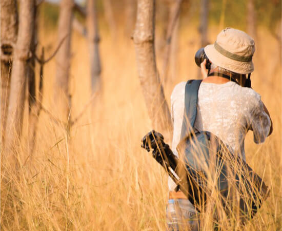 male tourist backpacker taking a photo near trees in Kenya Amboseli on 6-day Masai Mara Amboseli safari tours