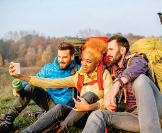 tres viajeros sentados en el suelo con grandes mochilas tomándose selfies en Masai Mara en safaris de 3 días