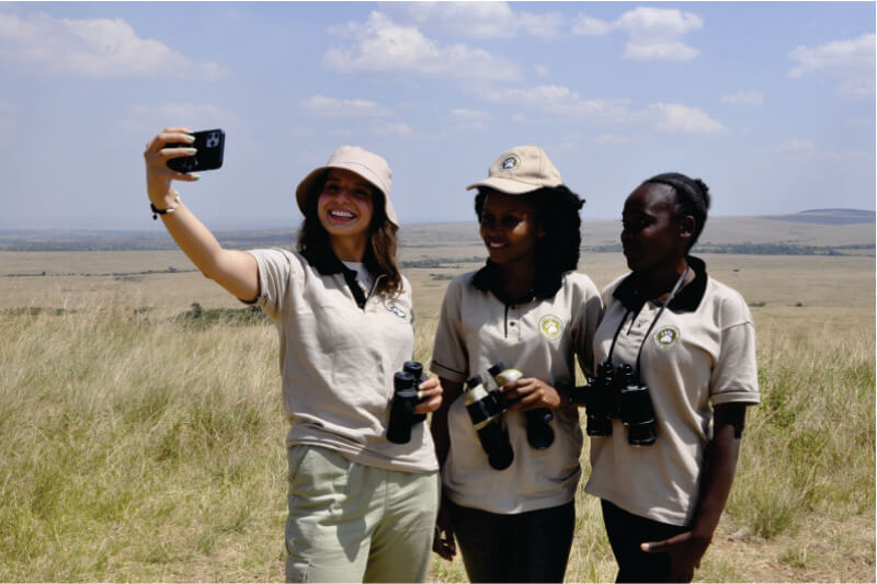 drie jonge gidsen van Bon Voyage Budget Safari in Kenia touroperator in bruin uniform met verrekijker en selfie makend