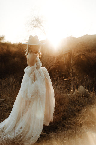 maternity photoshoot in a field in an ivory sheer dress covered in pearls with a wide brim hat
