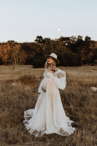 maternity photoshoot in a field in an ivory sheer dress covered in pearls with a wide brim hat