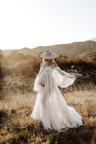 maternity photoshoot in a field in an ivory sheer dress covered in pearls with a wide brim hat