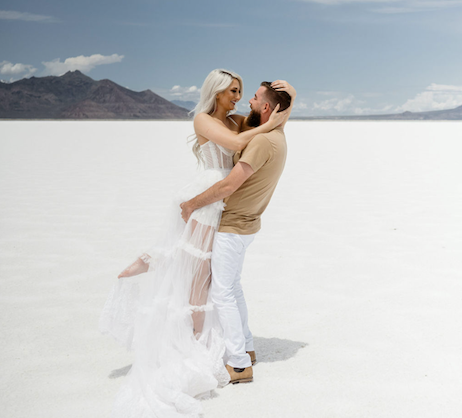 couple standing on the salt flats, man picked up and twirls woman in white lace dress