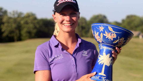 Bild på Madelene Sagström som håller upp en pokal på golfbanan.