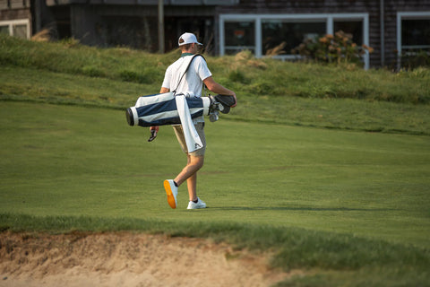Bild på ung man på golfbana med grönvit golfbag på axeln