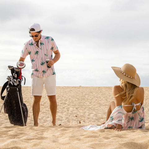 Two people on a sandy beach, one carrying a golf bag and wearing golf clothes