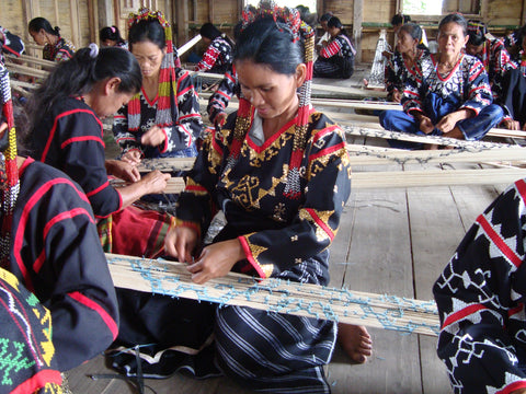 A group photo of several women of The T’boli Tribe in the Philippines weaving string to make fabric