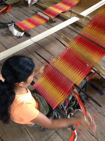 A photo of a woman of The T’boli Tribe in the Philippines weaving red and yellow string to make a patterned fabric