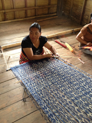 A photo of a woman of The T’boli Tribe in the Philippines weaving blue and white string to make a patterned fabric