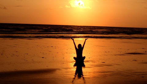 silhouette sitting on a beach with hands raised