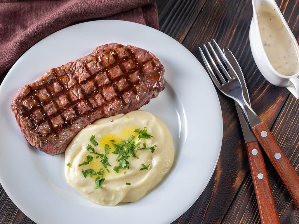 A plate with a Kansas City Strip Steak and side dishes