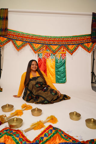 Kim Kalanduyan is sitting in the center of a white photo background surrounded by scattered kulintang gongs and colorful Maguindanaoan decorative drapery.