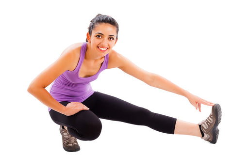 Woman stretching her leg while smiling, wearing a purple tank top and black leggings.