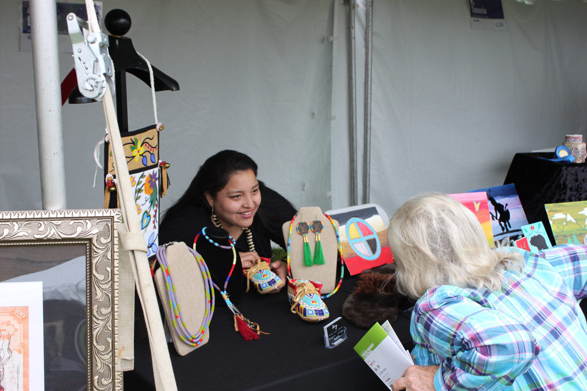 Indian Market and Festival artist Alexa Rae Day, Anishinaabe Hochunk Lakota, shows her work to a market visitor in 2019