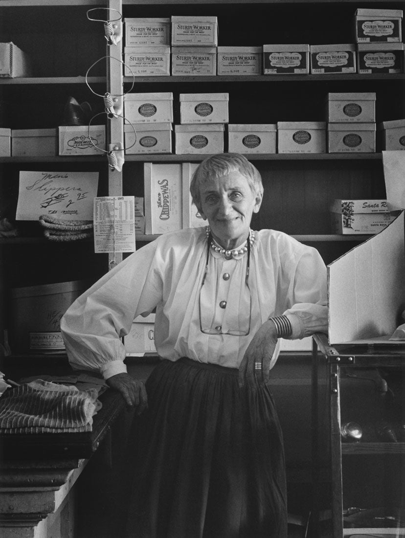 Pirkle Jones, ‘Dorothea Lange in McKenzie’s Store,’ 1956, 8 x 10. ” © Regents of the University of California, Courtesy of Special Collections & Archives. University Library, U.C. Santa Cruz. Ruth-Marion Baruch and Pirkle Jones Photographs and Papers.