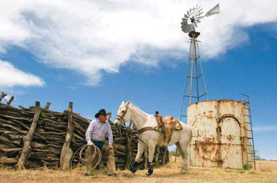 Fred and his favorite roping horse, Eagle, in front of his authentic style mesquite corral. The ranch’s windmill is visible in the background. Photography by Valerie Hayken Photography and Design.