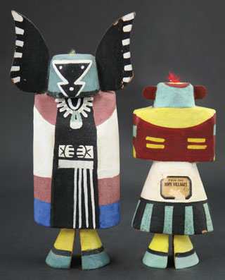 Hopi Kachina Tourist Dolls. The kachina on the left is Angwusnasomtaqa, or Tumas Crow Mother. She wears a woman's dress and ceremonial robe with green moccasins. She appears in the Bean Dance and is considered the mother of all the kachinas by some Hopi. Her Hopi name literally means "Man with Crow Wings Tied To." The kachina on the right is I'she, or the Mustard Green Kachina. This kachina has a green mask with red ears, black warrior marks on the cheeks, rectangular eyes, and a triangular mouth.