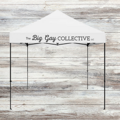 White pop up tent with The Big Gay Collective written in black on the valance on a grey wood background