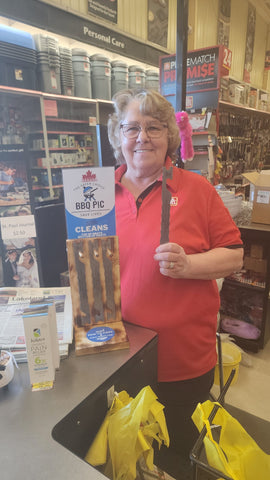 BBQ-Bilder zum Verkauf bei Home Hardware in St. Paul, Alberta, Kanada. Die BBQ-Bilder sind auf einer Holzpräsentation zu sehen. Die freundliche Kassiererin Irene hält ein BBQ-Foto in der Hand.