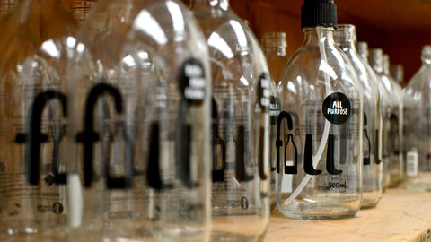 Glass bottles on a shelf with various product descriptions & 'Fill' logo, the 'i' of which is a drawing of a part empty bottle ready to be refilled