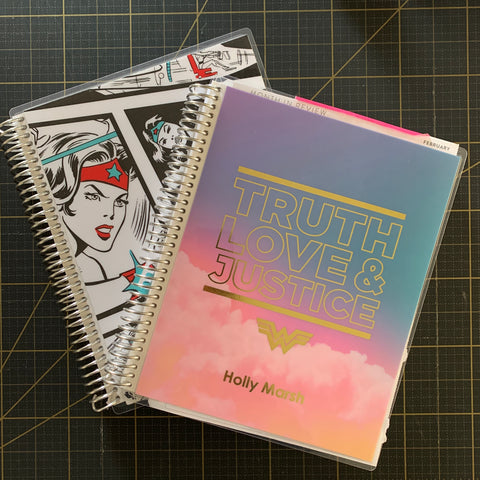 image of two Erin Condren coiled notebooks with Wonder Woman designs on their covers on a dark grid background