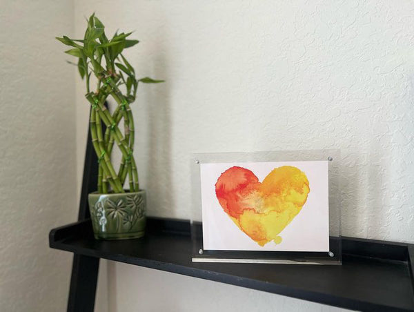 Postcard in a clear acrylic frame on a shelf with a bamboo plant