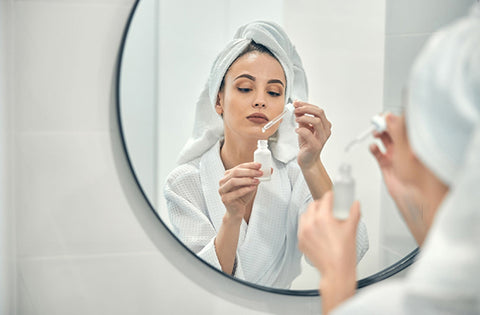 lady is applying kumkumadi serum infront of mirror