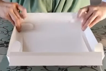 Hands folding the edges of a white paper box.