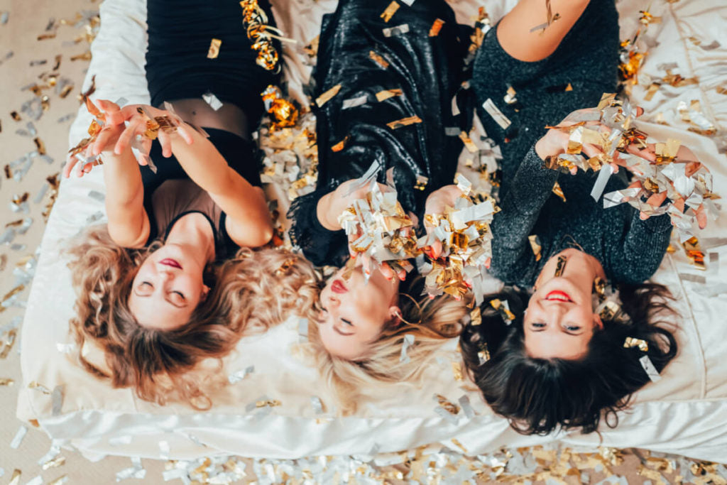 Three women lying down with confetti falling on them.