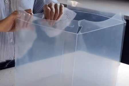 Two hands peeling off a clear film from the edge of a transparent box.