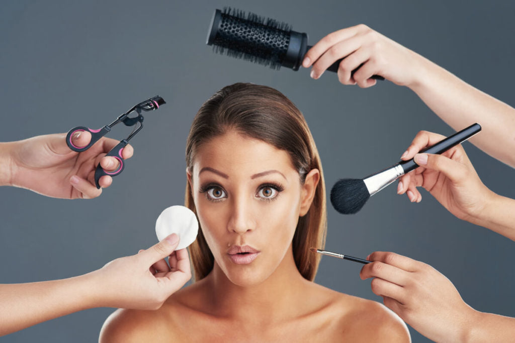 A woman, visibly surprised, finds herself surrounded by a team providing extensive assistance with her makeup.