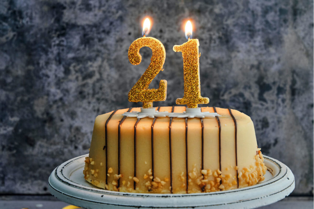 A birthday cake with golden '21' candles and dripping icing.