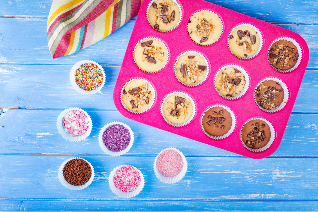 Colorful baking ingredients and cupcake liners on a blue wooden surface.