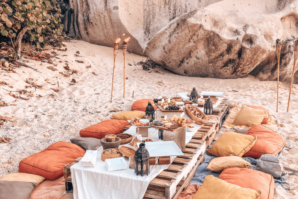 Beach picnic with decorated woooden table, pillow, foood and other snacks.