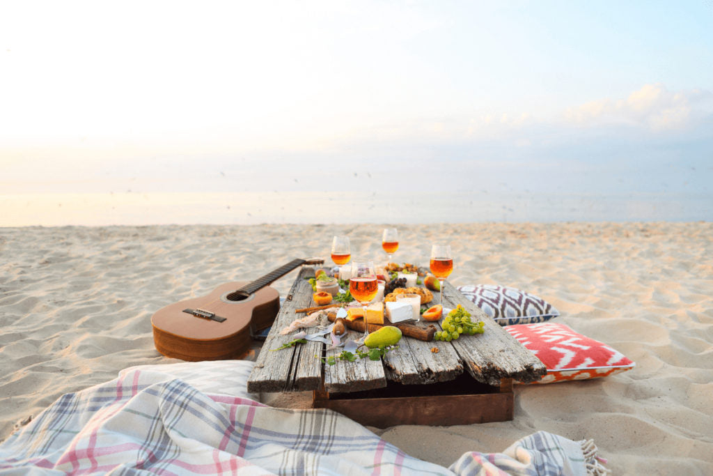 Picnic on the beach with wooden table, blankets, pillows and guitar.