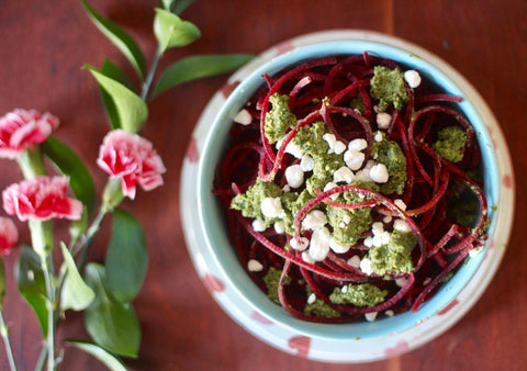 A bowl of beet noodles with goat cheese next to a bunch of pink flowers