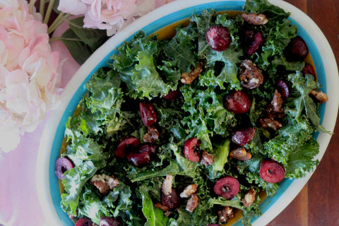 A bowl of kale salad topped with red cherries and pecans