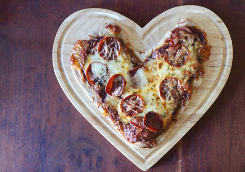 A heart-shaped pizza with pepperoni on a heart-shaped cutting board