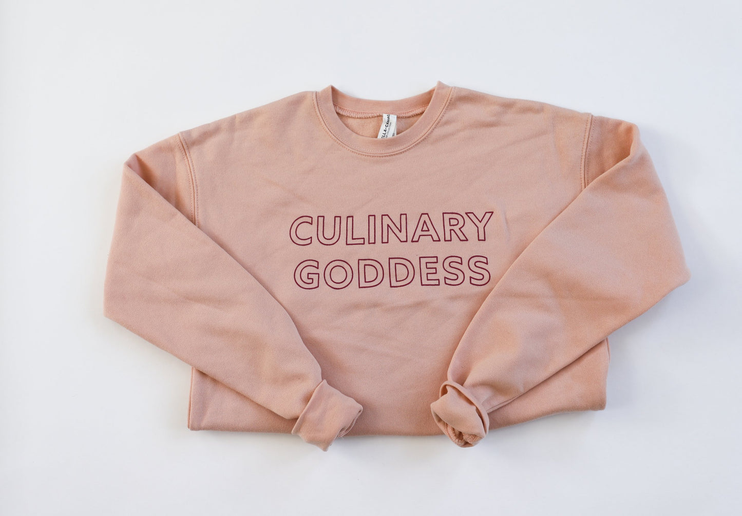 Peach colored crewneck sweatshirt with "Culinary Goddess" in pink block letters