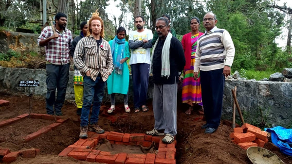 Kane standing next to his biodynamics teacher in Southern India. They are standing behind a preparation site where they are preparing cow horns for biodynamic use. They are in front of a small group of 7 people