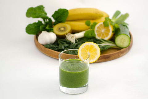 A glass of green juice with a lemon wedge on top of it