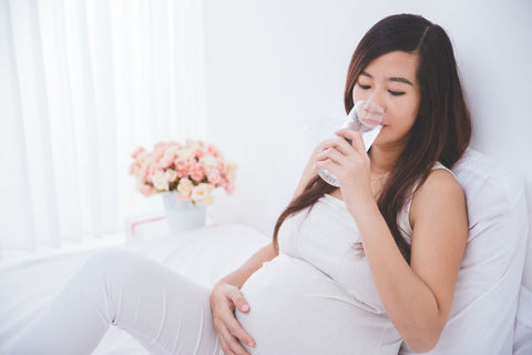 A pregnant person drinking alkaline water from a bottle